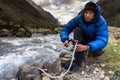 Man in blue down jacket filtering drinking water from a mountain river in Peru