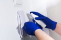 Man in blue gloves cleaning door phone with sanitizer
