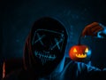 A man in a blue glowing mask holds a carved Halloween pumpkin lantern. A traditional symbol of the holiday. Creepy Halloween