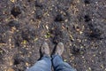 Man in blue jeans and trekking boots is standing on the burnt ground after fire.