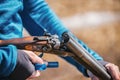 Man in a blue long sleeve shirt reloads an antique rifle outdoors