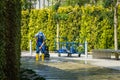 Man in blue overalls and yellow boots cleans granite bed of artificial fast river with car wash.