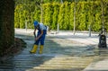 Man in blue overalls and yellow boots cleans granite bed of artificial fast river with car wash. Public landscape city park Krasno