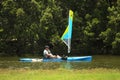 man on a blue peddle kayak with a small sail.