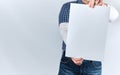 man in a blue plaid shirt and jeans is holding a blank rectangular white paper sheet