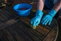 Man with blue rubber gloves is cleaning a dark wooden garden table at the beginning of spring, copy space, selected focus