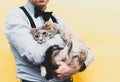 Man in blue shirt and black suspender holding cute sadness tabby grey cat on yellow