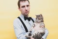 Man in blue shirt and black suspender holding cute tabby grey cat on back