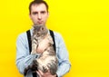 Man in blue shirt, black suspender holding grey striped tabby cat with outstretched paws and looking at camera