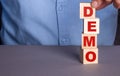 A man in a blue shirt composes the word DEMO from wooden cubes vertically