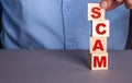 A man in a blue shirt composes the word SCAM from wooden cubes vertically