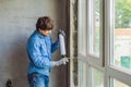 Man in a blue shirt does window installation. Using a mounting foam