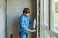 Man in a blue shirt does window installation. Using a mounting foam