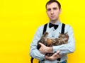 Man in blue shirt holding brown tabby cute cat and looking at camera in front of yellow Royalty Free Stock Photo