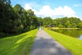 A man in a blue shirt running next to a couple with a dog walking down a smooth footpath next to the lake