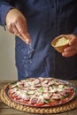 Man in a blue shirt sprinkle with cheese pizza from a ceramic sauser