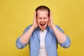 A man in a blue shirt on a yellow background holds his hands near his head, depicting a loud scream from different thoughts