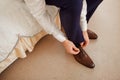 A man in a blue suit ties up shoelaces on brown leather shoes brogues on a wooden parquet background Royalty Free Stock Photo