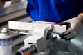 A man in a blue T-shirt and gray gloves clamps a part in a vice, a worker at a workbench