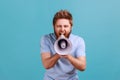 Man in blue T-shirt holding megaphone near mouth, loudly speaking, screaming, making announcement. Royalty Free Stock Photo