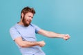 Man in blue T-shirt pretending to pull invisible rope, holding something heavy.