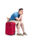 Man in a blue T-shirt and white shorts sits on a chair near a red suitcase, waiting. Isolated on white background Royalty Free Stock Photo