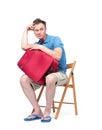 Man in a blue T-shirt and white shorts sits on a chair near a red suitcase, waiting. Isolated on white background Royalty Free Stock Photo