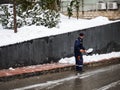 A man in a blue uniform removes a shovel of snow from the pavement Royalty Free Stock Photo