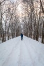 Man in blue walking alone on snow trail under tall tree canopy in winter