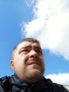 A man in a blue windbreaker against the blue sky with clouds looks into the distance