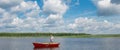 A man in a boat, in the center of the lake, holds a fishing pole to catch a big fish, against a beautiful sky Royalty Free Stock Photo