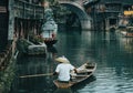Man in a boat with a traditional triangular chinese hat standing in waters of Tuo river flowing through the centre of ancient city Royalty Free Stock Photo