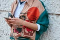 Man with bomber jacket in beige, green and orange looking at smartphone before Prada fashion show, Milan