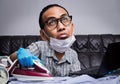 Man with boring face working with very busy business and housework part, ironing, working with laptop during self isolation Royalty Free Stock Photo