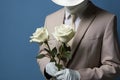 A man with a bouquet of roses in a suit and an incognito hat, blue background, mystery concept Royalty Free Stock Photo