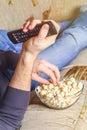 A man with a bowl of popcorn and a remote control in his hand looks at the TV on the sofa. Royalty Free Stock Photo