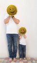 Man and boy holding yellow sunflower head in front of faces, on which muzzle with smile is drawn Royalty Free Stock Photo