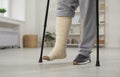 Man with broken leg in cast walking with crutches at home