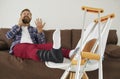 Man with broken leg, injured foot, or sprained ankle sitting on sofa and talking on mobile phone Royalty Free Stock Photo