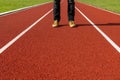 Man in brown sneakers and black jeans standing on a red running track.Front view