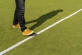Man in brown sneakers and black jeans stepping across a white line on a green surface