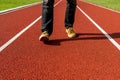 Man in brown sneakers and black jeans stepping forward on a red running track