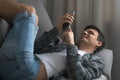 Man is browsing smartphone finding a woman on dating site online lying on sofa.