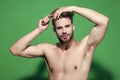 Man brush hair with hairbrush on green background. Guy with sexy torso, haircut. Beauty, grooming, hygiene. Health