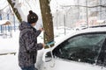 A man brushes snow from a car after a snowfall. Road safety, difficult weather conditions in winter