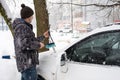 A man brushes snow from a car after a snowfall. Road safety, difficult weather conditions in winter