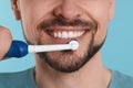 Man brushing his teeth with electric toothbrush on light blue background, closeup Royalty Free Stock Photo