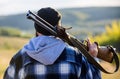 Man brutal guy gamekeeper in hat nature background. Brutality and masculinity. Hunter carry rifle gun on shoulder rear Royalty Free Stock Photo