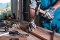 A man Builder in overalls and gloves hammers a nail into a wooden Board close-up, roof, construction, home workshop