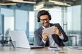 A man in a business suit and headphones is playing a game on a tablet computer inside the office, an arab is smiling